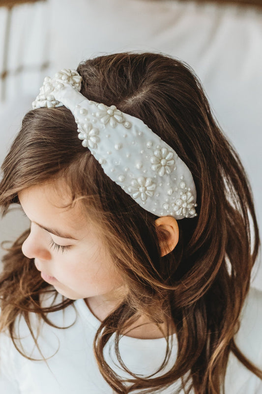 The Daisy Pearl Headband is white satin with pearls in assorted sizes.  The pearls make daisy flower shapes and are spread around on both sides.  This hair accessory is designed for all day comfort and is give any outfit an added touch of glamour. 