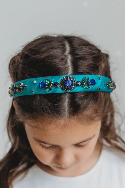 The Arabian Princess Headband is a bright teal with royal blue and emerald green jewels.  They are designed in ornate patterns.  The headband is approximately an 1" wide. 