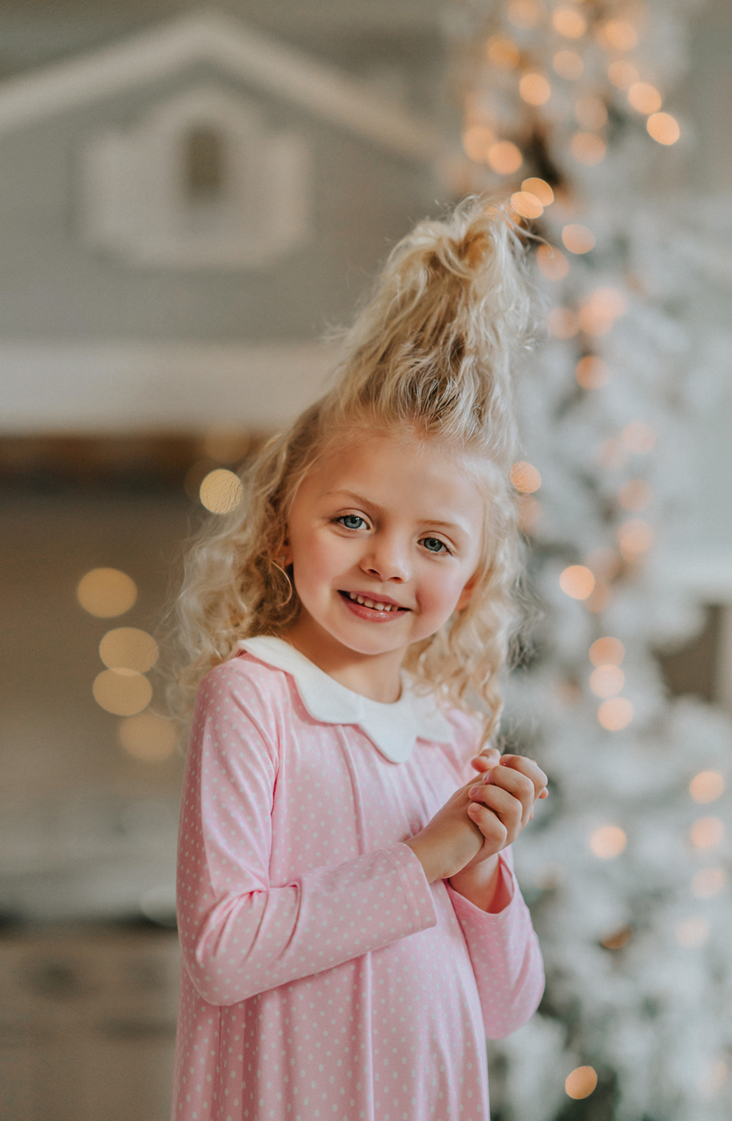 A young girl is wearing the Sleepy Who Gown inspired by Cindy Lou Who.  The buttery soft lounge wear has a white collar.  Light pink with small white polka dots and two adorable ruffles at the bottom. 