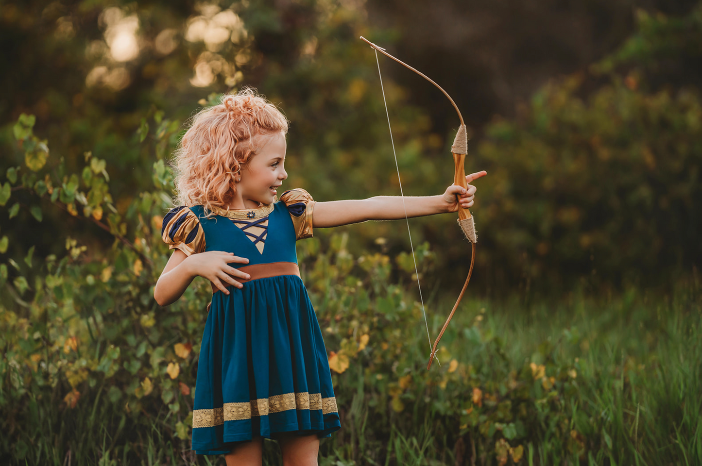 A young girl is wearing a dark teal cotton twirl dress.  The puff sleeves have metallic gold.  Metallic gold lines the neck with a dark teal jewel.  A intricate gold ribbon runs along the hem. 