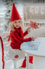 A young girl is wearing a red pointy gnome hat with a white round shape skirt. There are red snowflake applique around the bottom of the skirt.