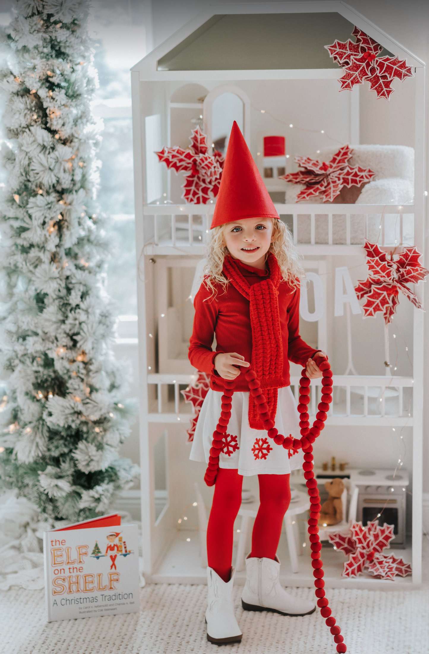 A young girl is wearing a red pointy gnome hat with a white round shape skirt. There are red snowflake applique around the bottom of the skirt.