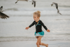 A young girl is wearing a 2 piece long sleeve rash guard swim set. The top is black with turquoise and goldenrod accents. The bottom has a turquoise ruffle over a mint teal skirt with goldenrod hem accent. 