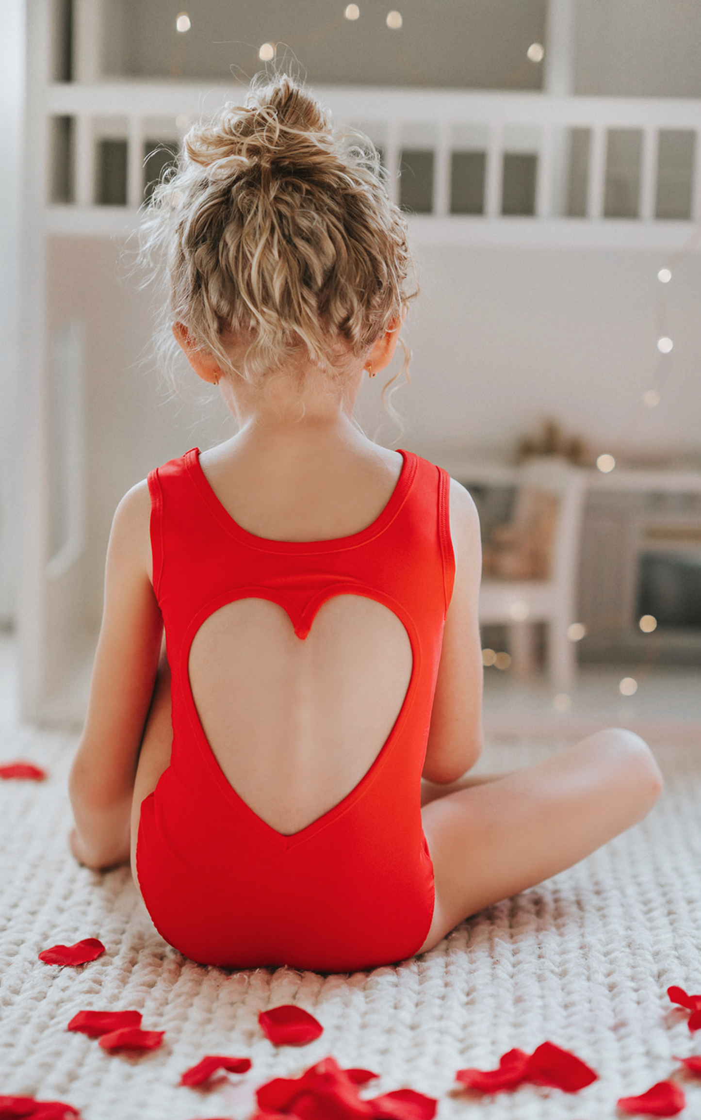 A young girl is wearing the Love Bug Leotard, a red gymnastics outfit with an elegant heart cutout back. 