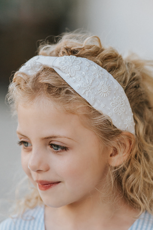 The Micro Beaded Floral Celebration Headband is white with small white white beads in various shapes.  They are sewn in floral patterns and scattered to cover the headband. This hair accessory is designed for all day comfort. 