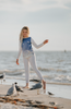 A young girl is wearing a stylish Seagull Soundtrack Shirt with a blue front panel featuring birds in flight, crafted from soft cotton jersey knit, paired with white leggings. 