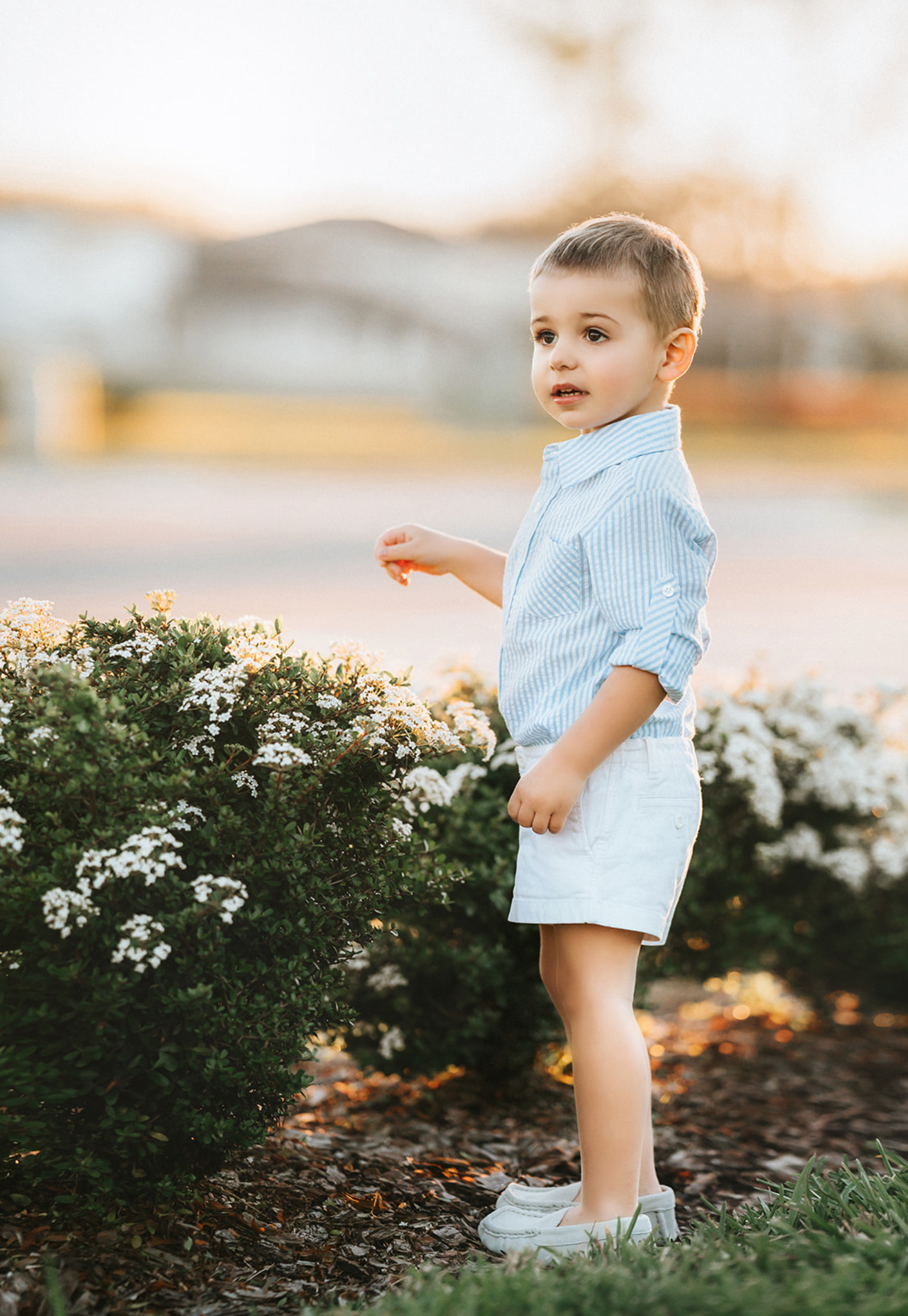 A young boy wears a long sleeve button up collared shirt. A light blue and white vertical seersucker shirt with a pocket on the left chest. 