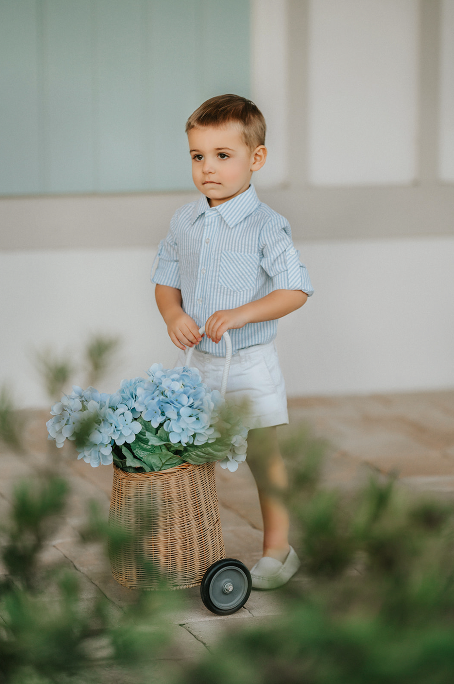 A young boy wears a long sleeve button up collared shirt. A light blue and white vertical seersucker shirt with a pocket on the left chest. 