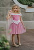 A young girl in an exquisite Portrait Petite Sleeping Beauty twirl length gown poses in a castle setting.  The pink stretch velvet gown has an off the shoulder neckline with two straps.   The pink tulle skirt is full and has a cotton liner for comfort.