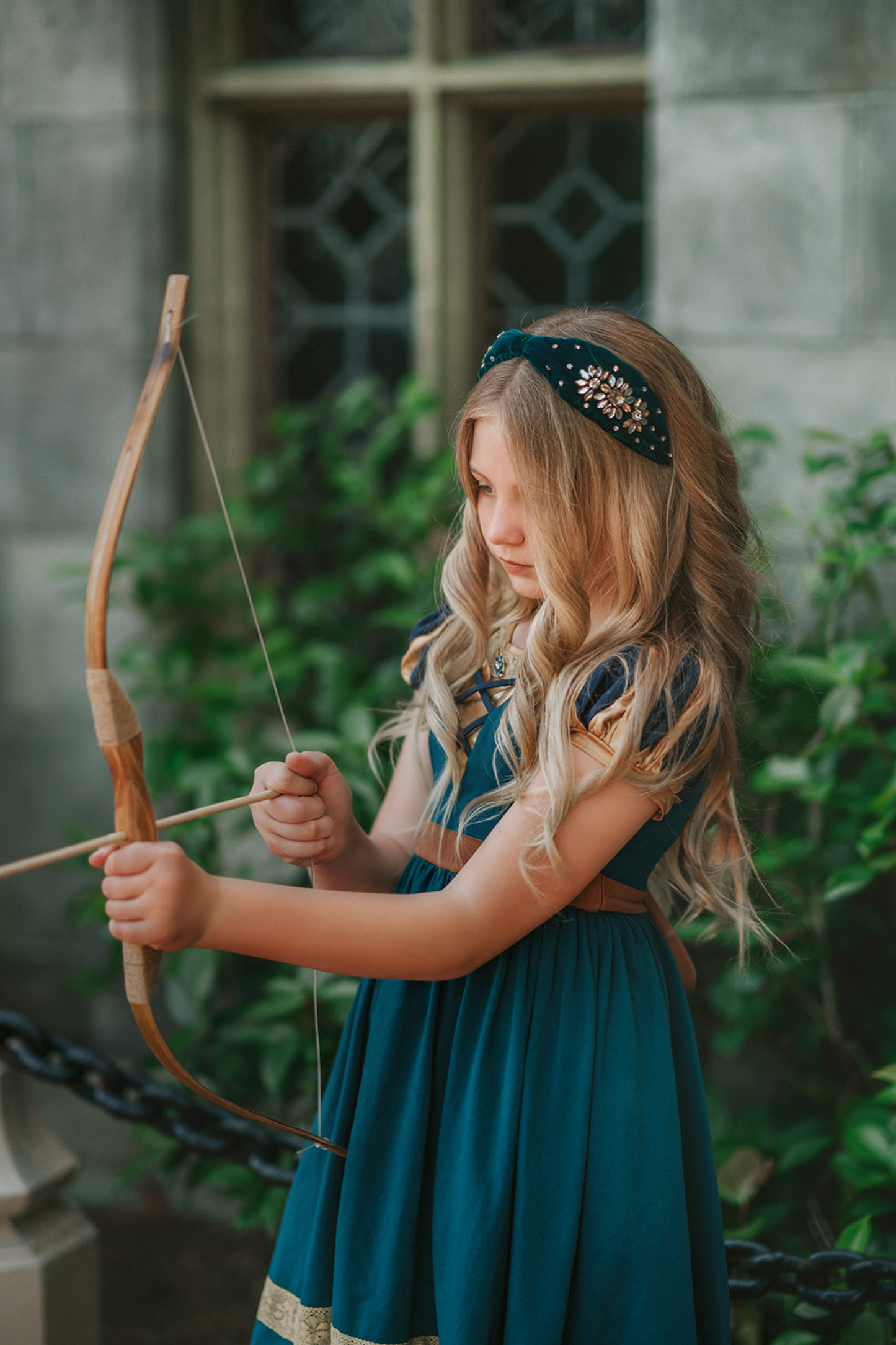 A young girl is wearing a dark teal cotton twirl dress.  The puff sleeves have metallic gold.  Metallic gold lines the neck with a dark teal jewel.  A intricate gold ribbon runs along the hem. 