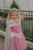 A young girl in an exquisite Portrait Petite Sleeping Beauty twirl length gown poses in a castle setting.  The pink stretch velvet gown has an off the shoulder neckline with two straps.   The pink tulle skirt is full and has a cotton liner for comfort.