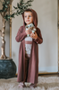 A young boy is wearing a buttery soft brown robe with hood. The robe is ankle length and open in the front.  The two piece pajama beneath has taupe pants and a short sleeve shirt with brown band across the waist. 