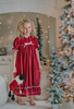 A young girl is wearing The Original Clara Nutcracker Gown in Merry Maroon, featuring maroon ruffles and an ivory bow. The buttery soft fabric is cozy and sensory friendly.  The puff sleeves with ribbon detail and the ruffles at the hem add a traditional classic look. 