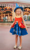 A young girl is wearing our Sorcerer Mouse Twirl Dress and Hat.  That wizard hat is blue with silver moon and stars.  The dress has a gold collar and red bodice.  The skirt has a gold rope bow and a metallic red bustle layer atop a blue twirl skirt. The skirt is adorned with a silver moon and stars. 