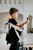 A young boy is seen standing indoors, wearing the black and silver Boys Bat Wing Shirt from the unisex collection. The shirt features a unique design that makes it look as if he has wings on his back. 