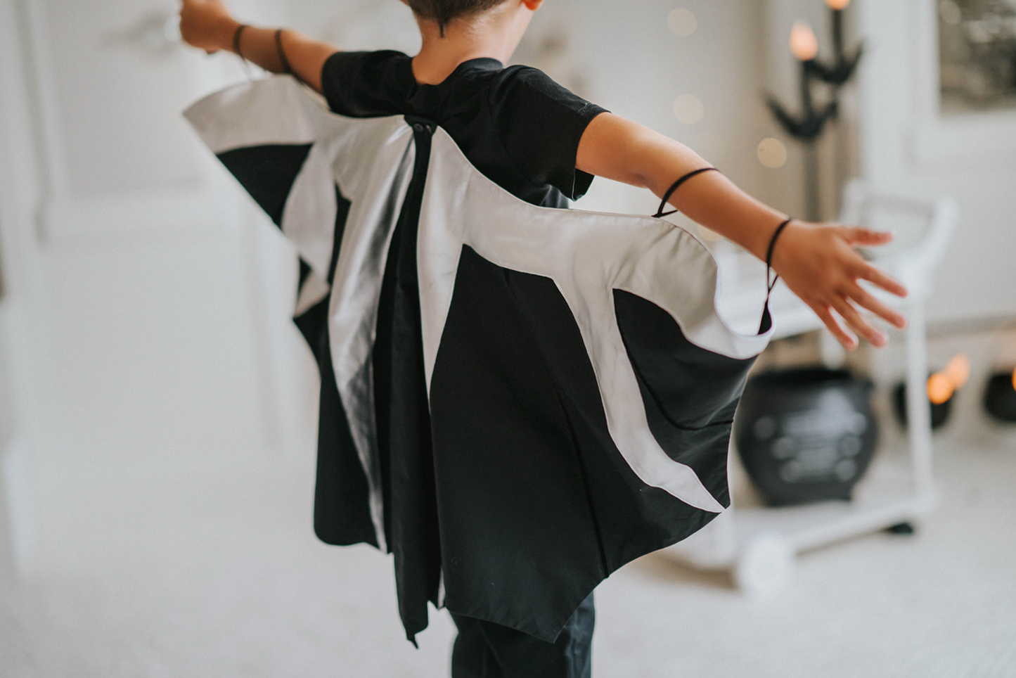 A child, viewed from the back, is wearing a Boys Bat Wing Shirt with outstretched arms to showcase the wing-like design of the cape. 