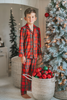 A young child in Unisex Pj's in Red Plaid decorates a Christmas tree. The plaid has green, white and black over a bright red.  The classic 2 piece pajamas have green piping and red buttons down the front of the shirt. 