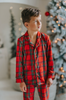 A young child in Unisex Pj's in Red Plaid decorates a Christmas tree. The plaid has green, white and black over a bright red.  The classic 2 piece pajamas have green piping and red buttons down the front of the shirt. 