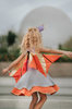 A young girl is wearing a light purple and heather grey cotton dress.  There is a light pink sparkle oval to resemble a belly.  The skirt is a double twirl with the second layer in orange.  The detachable wings are gold and orange. 