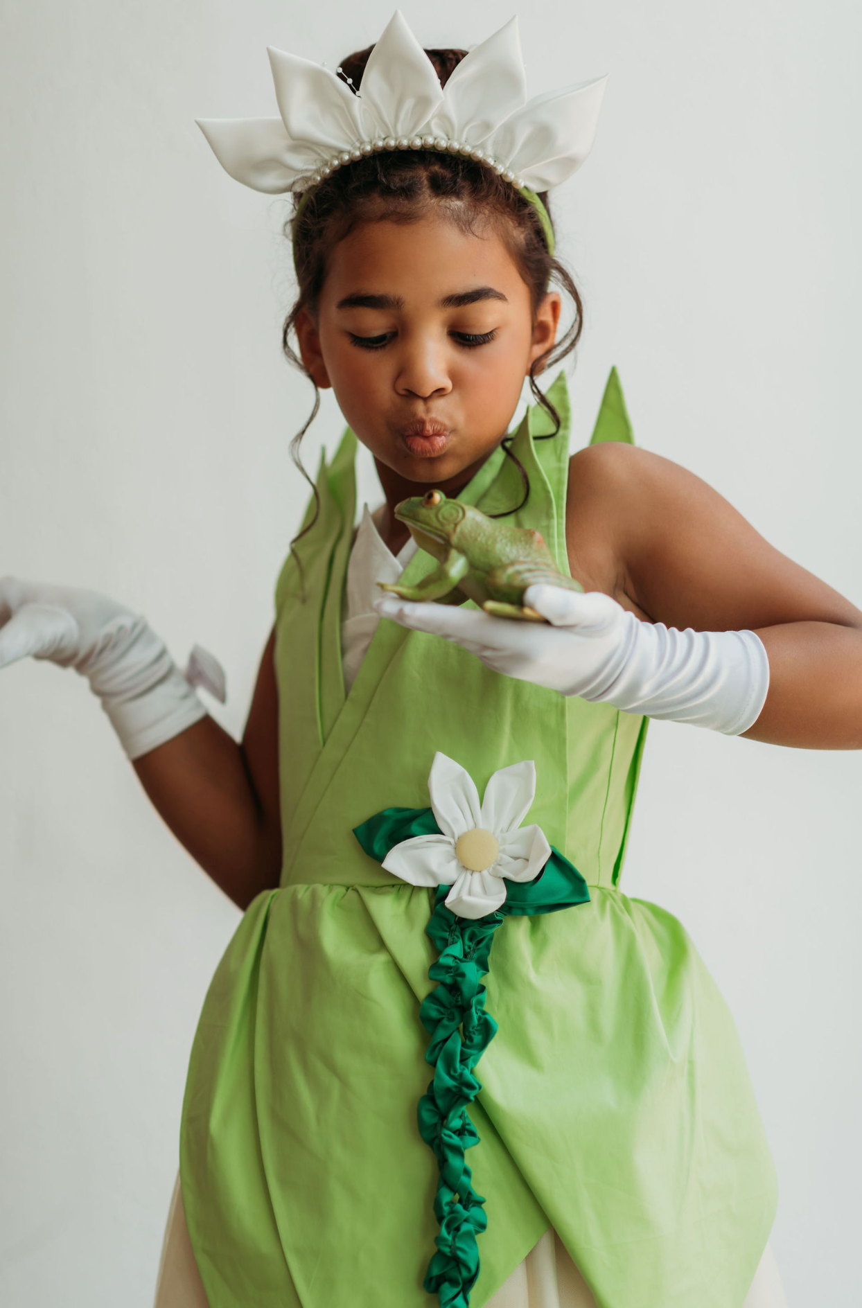 A young girl is wearing a beautiful bright green gown.  The layers on the bodice and skirt are cut like leaves.  There is a light yellow golden tulle skirt.   There is a magnolia flower with green leaves adorned on the side. 