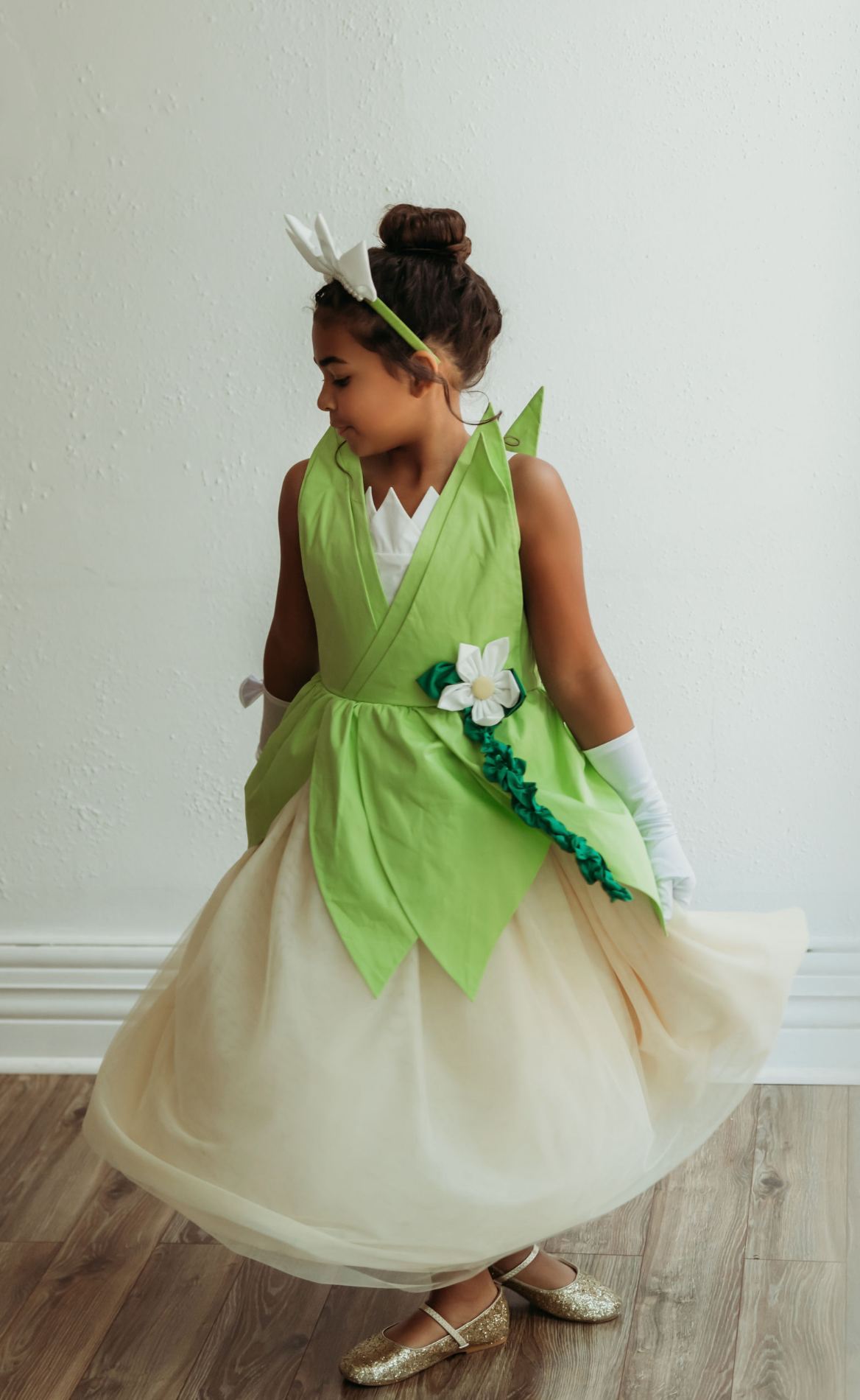 A young girl is wearing a beautiful bright green gown.  The layers on the bodice and skirt are cut like leaves.  There is a light yellow golden tulle skirt.   There is a magnolia flower with green leaves adorned on the side. 