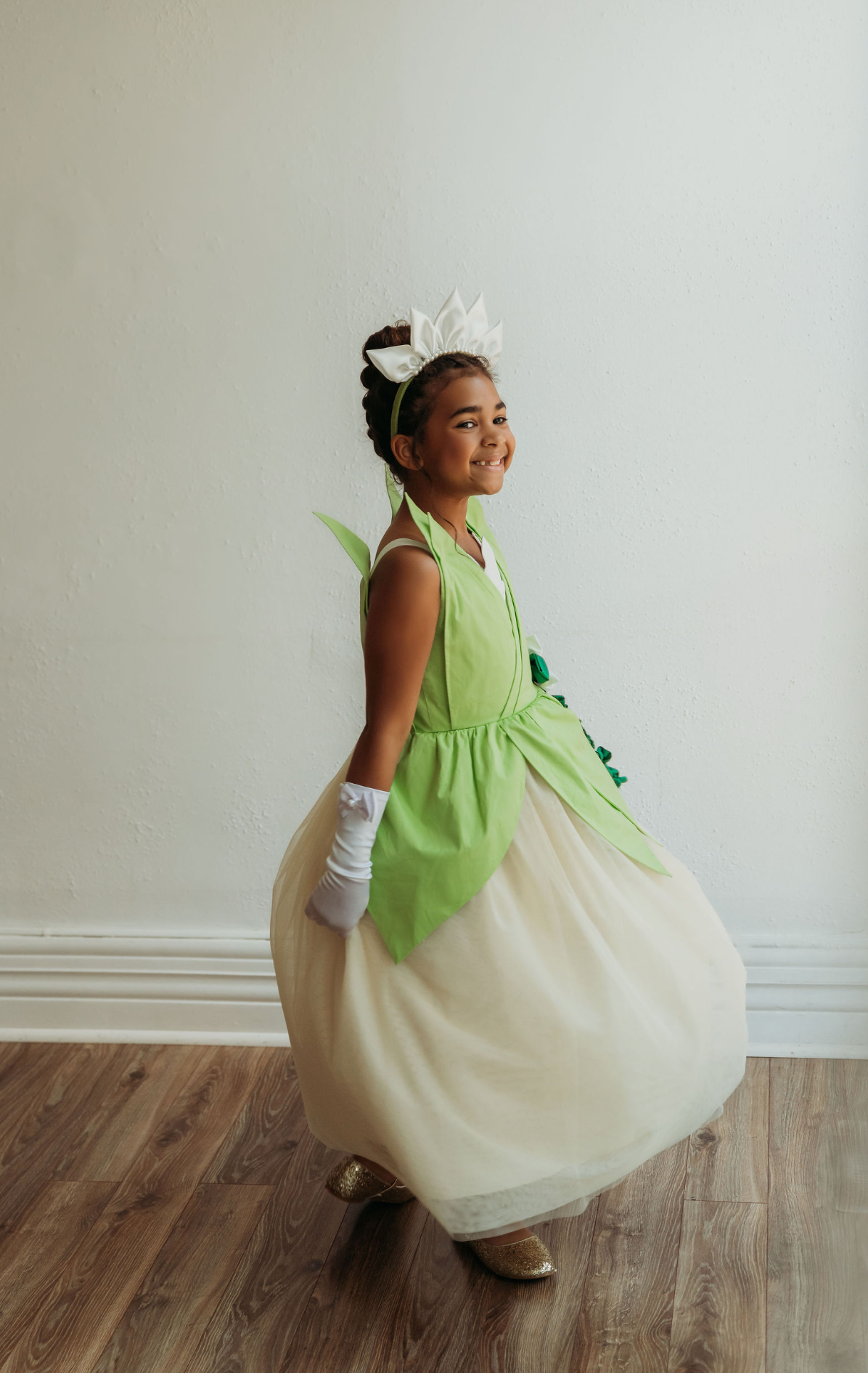 A young girl is wearing a beautiful bright green gown.  The layers on the bodice and skirt are cut like leaves.  There is a light yellow golden tulle skirt.   There is a magnolia flower with green leaves adorned on the side. 