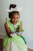 A young girl is wearing a beautiful bright green gown.  The layers on the bodice and skirt are cut like leaves.  There is a light yellow golden tulle skirt.   There is a magnolia flower with green leaves adorned on the side. 