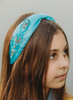 The Cinderella headband is a light satin blue.  The headband is designed for all day comfort.  There are gold, silver and light blue beads sewn in ornate designs on the left and right side. The middle is pulled together by a small flat ribbon. 