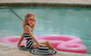 A young girl is wearing a black and white stripped one piece swim suit.  The white spaghetti straps are adjustable. The black and white pattern is in a chevron style.  A large floppy brimmed beach hat in matching black and white stripe is on her head. 