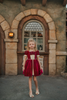 A young girl is wearing a twirl length gown inspired by our favorite red rose princess at Christmas.  The deep crimson red is stretch velvet.  The puff sleeves have a gold ruffle detail. Three chiffon roses line the neck and the bodice has gold inlay.  The skirt has gold inlay in a center pleat.  A stunning dress for any occasion. 