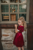 A young girl is wearing a twirl length gown inspired by our favorite red rose princess at Christmas.  The deep crimson red is stretch velvet.  The puff sleeves have a gold ruffle detail. Three chiffon roses line the neck and the bodice has gold inlay.  The skirt has gold inlay in a center pleat.  A stunning dress for any occasion. 