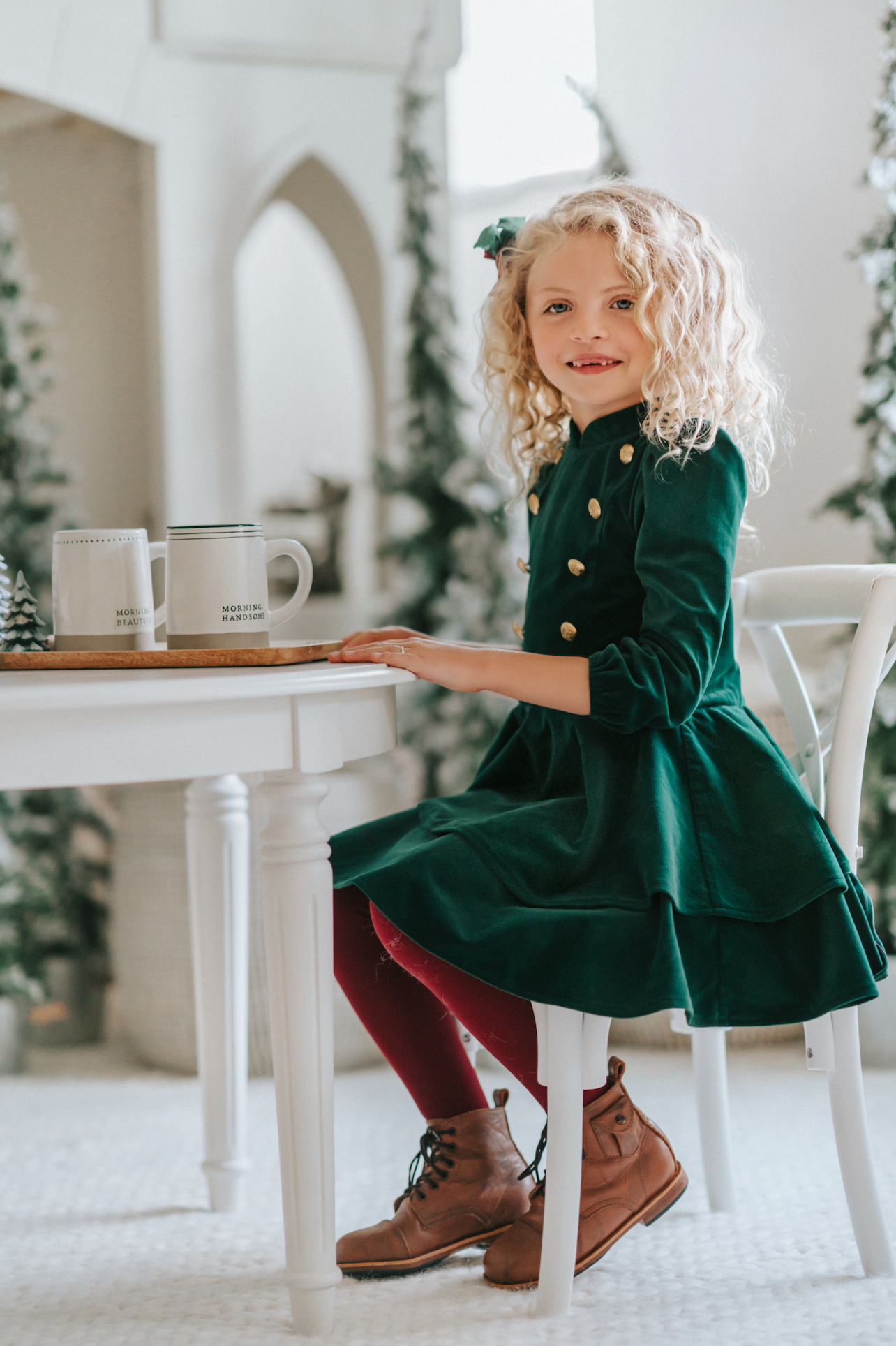 A young girl is wearing an evergreen velvet soldier twirl dress.  The deep velvet is stretchy and has a uniform collar with gold buttons down the bodice.  The 3/4 sleeves have elastic at the cuff.  There are two layers of velvet in the skirts. 