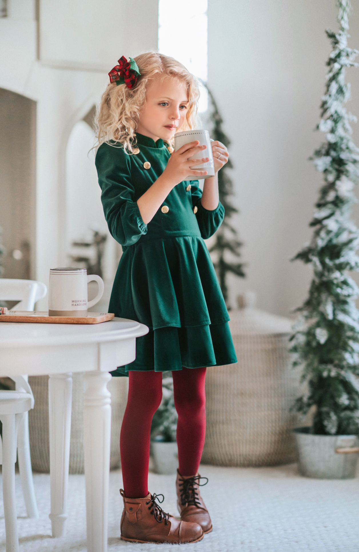 A young girl is wearing an evergreen velvet soldier twirl dress.  The deep velvet is stretchy and has a uniform collar with gold buttons down the bodice.  The 3/4 sleeves have elastic at the cuff.  There are two layers of velvet in the skirts. 