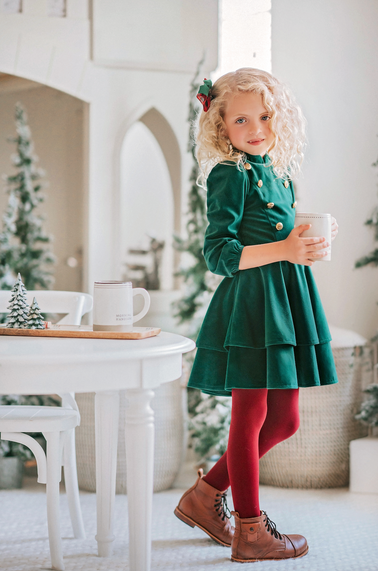 A young girl is wearing an evergreen velvet soldier twirl dress.  The deep velvet is stretchy and has a uniform collar with gold buttons down the bodice.  The 3/4 sleeves have elastic at the cuff.  There are two layers of velvet in the skirts. 