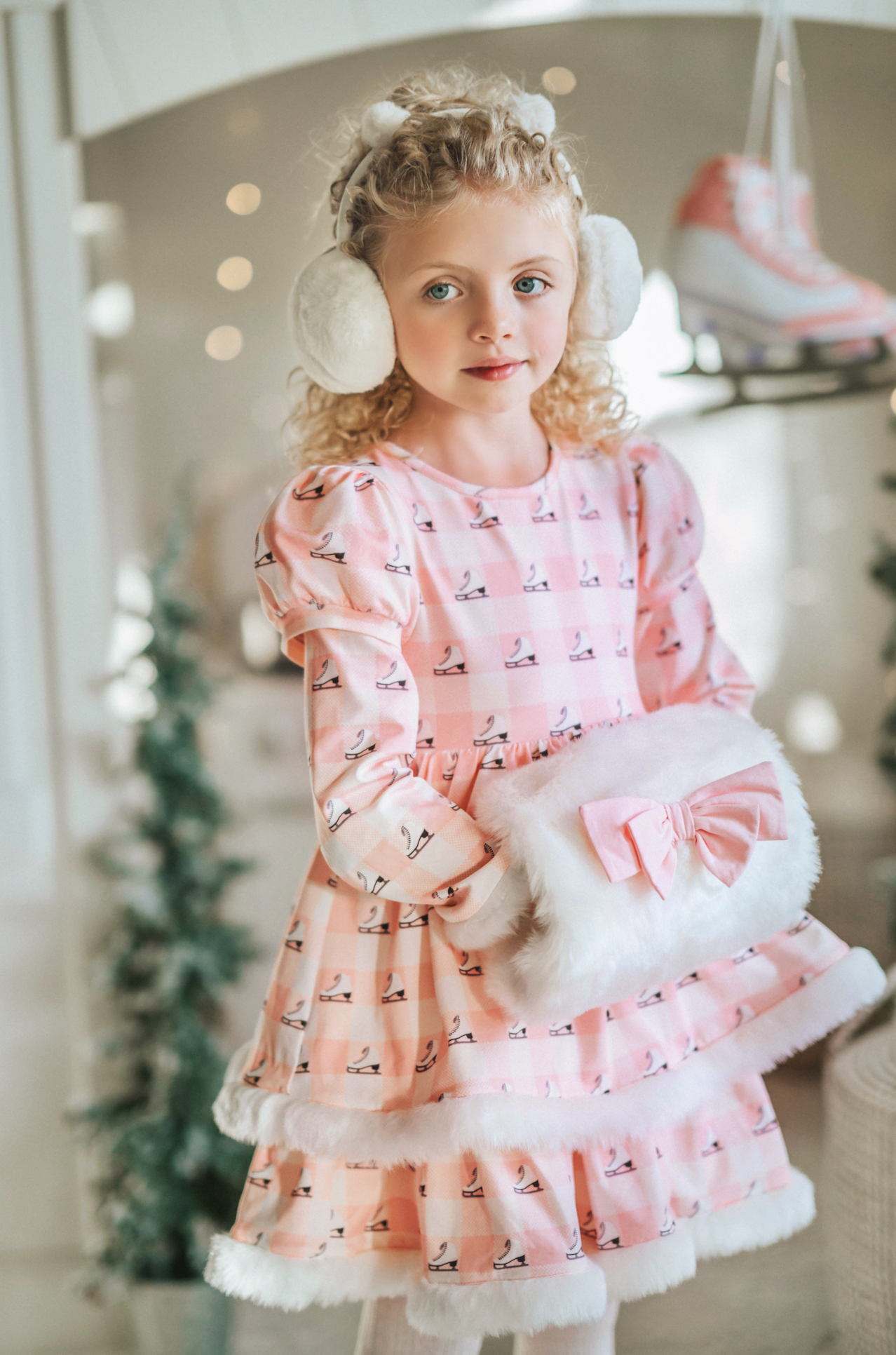 A young girl is wearing a long sleeve pink twirl dress adorned with white and silver ice skates.  The sleeves and hem of the twirl are lined with white faux fur.  There is a double layer skirt for excellent twirling.  Also included is a white faux fur hand muff with pink bow. 