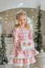 A young girl is wearing a long sleeve pink twirl dress adorned with white and silver ice skates.  The sleeves and hem of the twirl are lined with white faux fur.  There is a double layer skirt for excellent twirling.  Also included is a white faux fur hand muff with pink bow. 