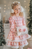 A young girl is wearing a long sleeve pink twirl dress adorned with white and silver ice skates.  The sleeves and hem of the twirl are lined with white faux fur.  There is a double layer skirt for excellent twirling.  Also included is a white faux fur hand muff with pink bow. 