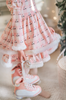 A young girl is wearing a long sleeve pink twirl dress adorned with white and silver ice skates.  The sleeves and hem of the twirl are lined with white faux fur.  There is a double layer skirt for excellent twirling.  Also included is a white faux fur hand muff with pink bow. 