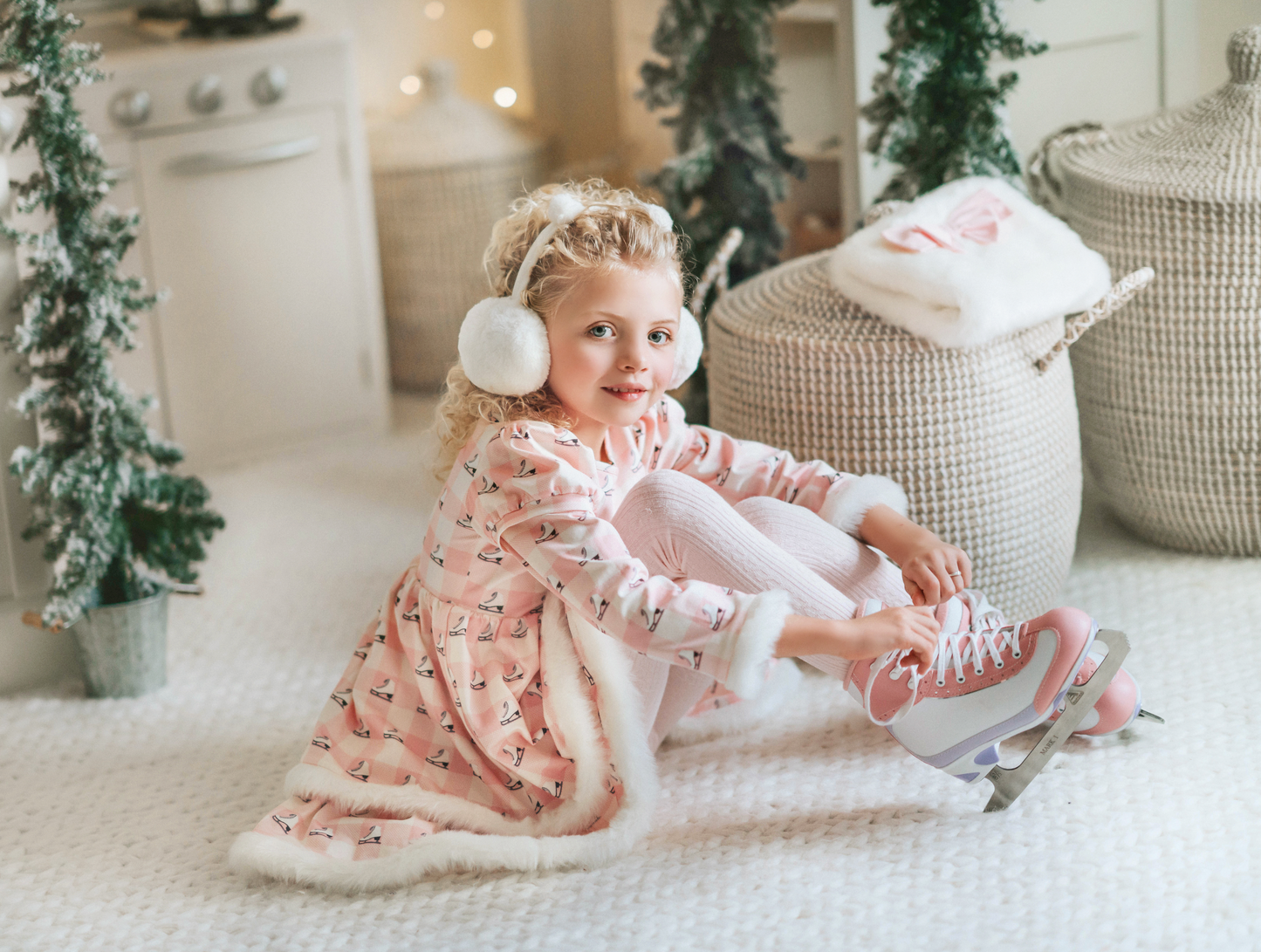 A young girl is wearing a long sleeve pink twirl dress adorned with white and silver ice skates.  The sleeves and hem of the twirl are lined with white faux fur.  There is a double layer skirt for excellent twirling.  Also included is a white faux fur hand muff with pink bow. 