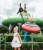 A young girl wears a sporty space hero twirl dress.  The cotton dress is sleeveless and has light green panels on the bodice with embroidered button like features.  There are light green and light purple racing stripes down the side. The front has two pockets on the skirt. 