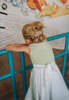 A young girl wears a sporty space hero twirl dress.  The cotton dress is sleeveless and has light green panels on the bodice with embroidered button like features.  There are light green and light purple racing stripes down the side. The front has two pockets on the skirt. 