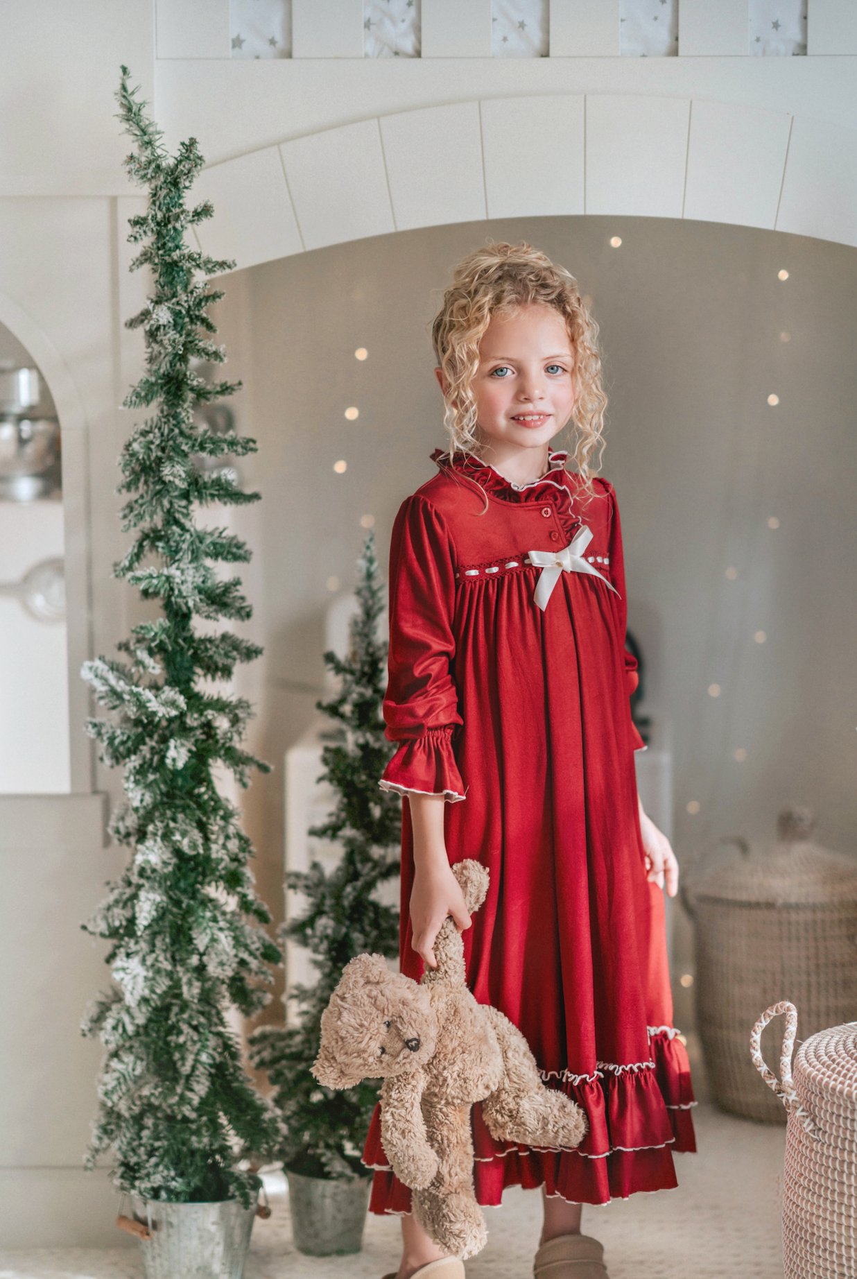 A young girl is wearing The Original Clara Nutcracker Gown in Merry Maroon, featuring an ivory bow. The buttery soft fabric is cozy and sensory friendly.  The long sleeves and the ruffles at the hem add a traditional classic look.