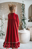 A young girl is wearing The Original Clara Nutcracker Gown in Merry Maroon, featuring an ivory bow. The buttery soft fabric is cozy and sensory friendly.  The long sleeves and the ruffles at the hem add a traditional classic look.