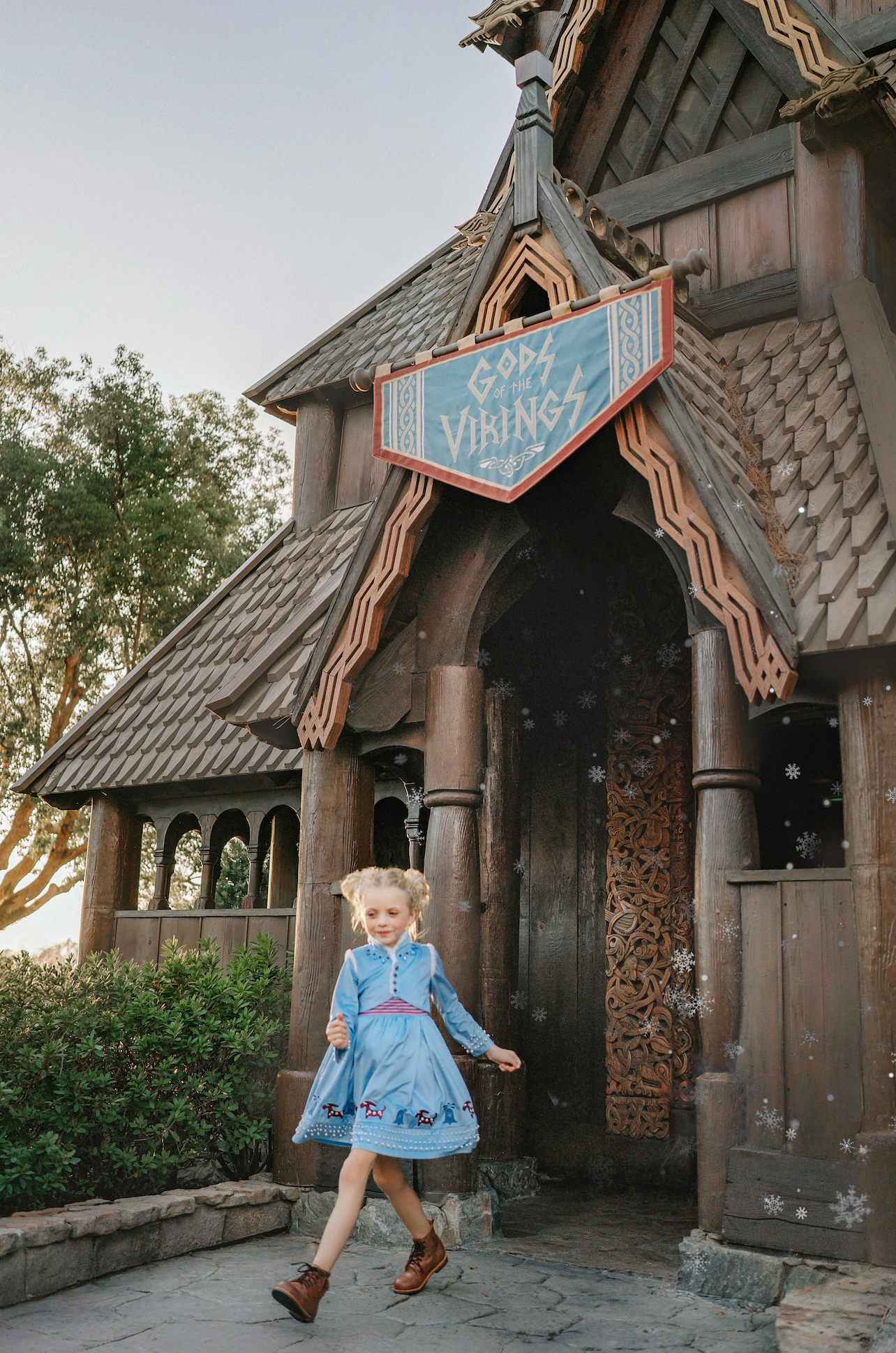 A young girl is wearing a beautiful blue velvet dress.  There is white faux fur trim on the collar and attached jacket. Adorned with blue and purple crystal gems and intricate buttons. The bottom of the dress has a blue bell and Scandinavian mountain goat applique. There are three rows of pearls on the sleeves and the hem of the skirts. 