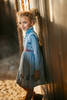 A young girl is wearing a beautiful blue velvet dress.  There is white faux fur trim on the collar and attached jacket. Adorned with blue and purple crystal gems and intricate buttons. The bottom of the dress has a blue bell and Scandinavian mountain goat applique. There are three rows of pearls on the sleeves and the hem of the skirts. 