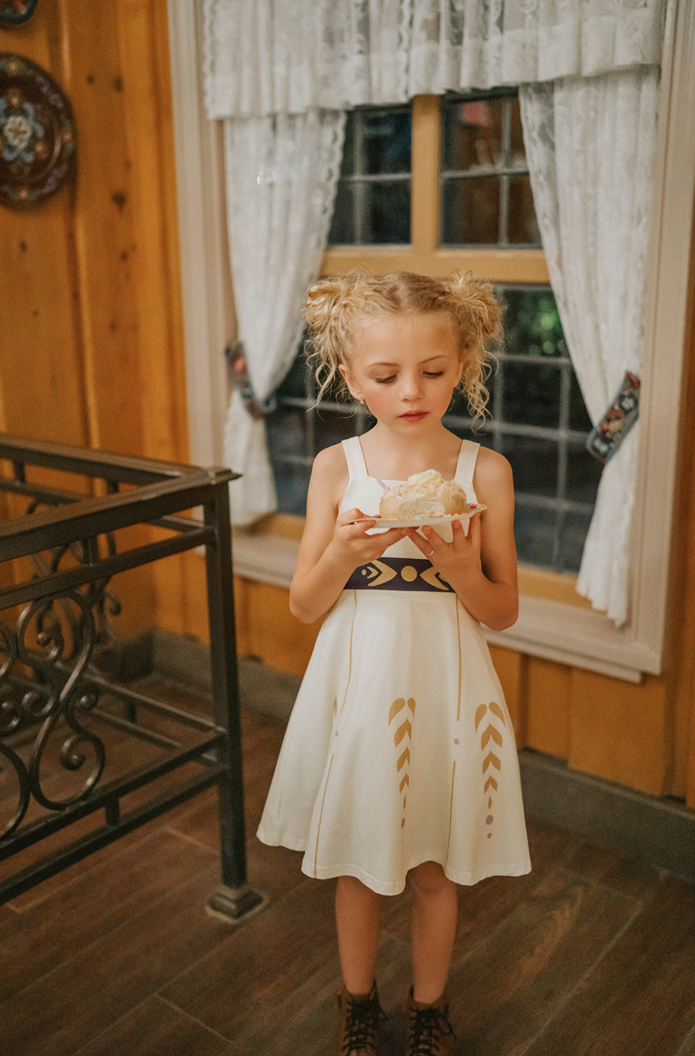 A young girl stands wearing a cotton twirl dress. There is sewn in petti skirt for volume. A geometric golden detail adorns the ivory dress.  There is a purple band with tie at the waist.  The sleevless dress comes with a golden yellow bolero with print on the front in true Arendale princess fashion.