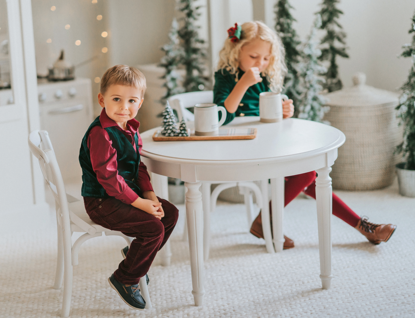 A young boy is with his sibling. He is wearing an evergreen velvet vest with three flat gold buttons.  There is a small pocket on the left chest.  The back has an adjustable buckle to that tightens.  A young girl is wearing the matching evergreen velvet soldier dress. 