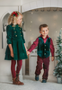 A young boy is with his sibling. He is wearing an evergreen velvet vest with three flat gold buttons.  There is a small pocket on the left chest.  The back has an adjustable buckle to that tightens.  A young girl is wearing the matching evergreen velvet soldier dress. 