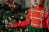 A young girl is wearing a toy soldier twirl dress.  The military collar leads into a cotton bodice adorned with gold thread detail that resembles a soldier uniform.  The evergreen chiffon skirt has multiple layers and is hemmed with gold.  The long sleeve dress is perfect for family holiday photos. 