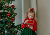 A young girl is wearing a toy soldier twirl dress.  The military collar leads into a cotton bodice adorned with gold thread detail that resembles a soldier uniform.  The evergreen chiffon skirt has multiple layers and is hemmed with gold.  The long sleeve dress is perfect for family holiday photos. 